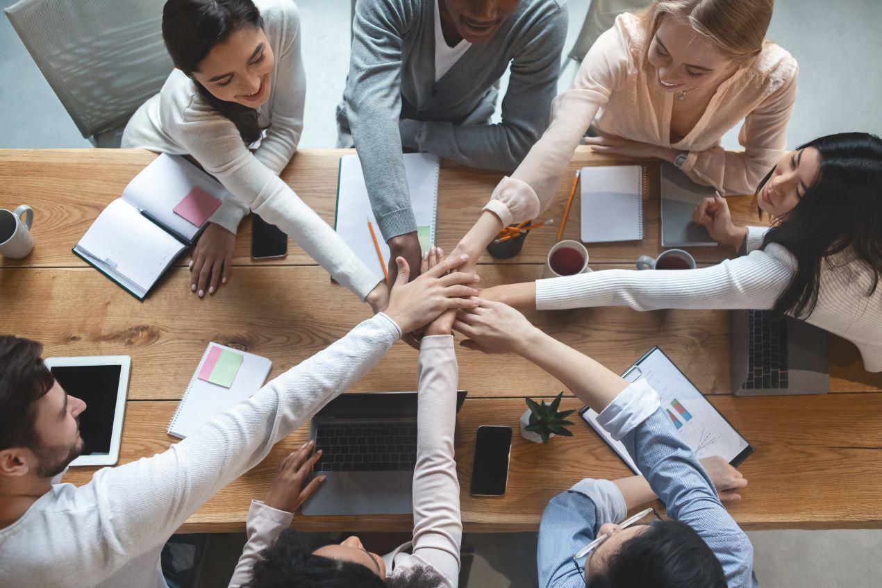 Ein motiviertes Team in einer Besprechung, das Hände zusammenlegt – Symbol für Zusammenarbeit und die Arbeit einer Employer Branding Agentur.